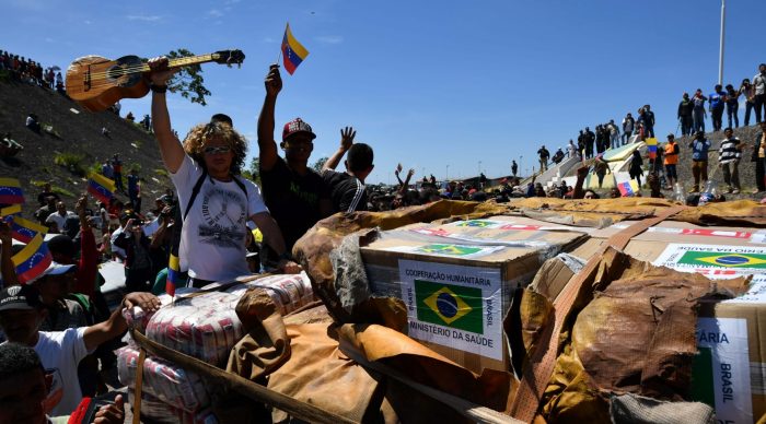 People cheer as trucks with humanitarian aid to Venezuela approach the Brazil-Venezuela border in Pacaraima, Roraima state, Brazil on February 23, 2019. – Venezuela braced for a showdown between the military and regime opponents at the Colombian border on Saturday, when self-declared acting president Juan Guaido has vowed humanitarian aid would enter his country despite a blockade. Early Saturday two large trucks -driven by Venezuelans and escorted by Brazilian police- carrying eight tonnes of emergency aid left Boa Vista in Brazil en route to the Venezuelan border. (Photo by Nelson Almeida / AFP)