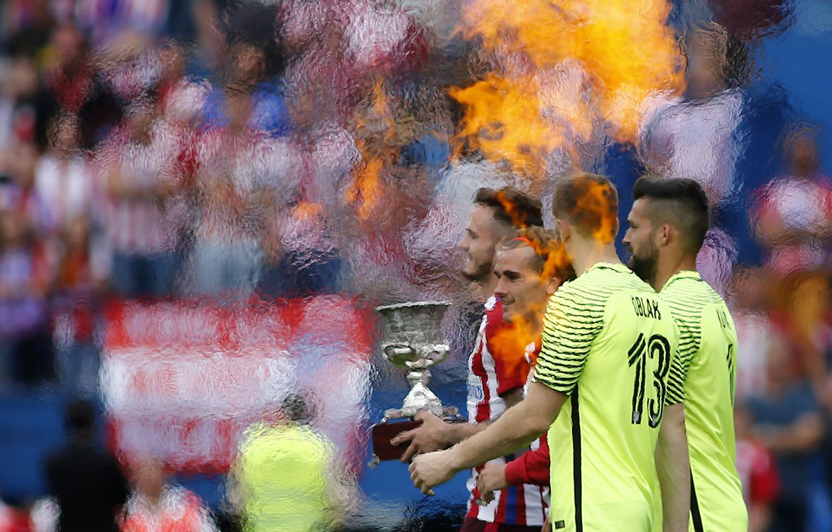 Atletico de Madrids French forward Griezmann (C) carries a trophy as he walks between flames during a celebration bidding farewell to the teams stadium after the Spanish league football match Club Atletico de Madrid vs Athletic Club Bilbao at the Vicente Calderon stadium in Madrid on May 21, 2017. - Atletico Madrids mythical Vicente Calderon stadium will soon be history: sad news for supporters of Real Madrids rivals but not so for locals who hope the neighbourhood will improve once noisy fans are gone. This weekend spells the end for the ageing structure that for over 50 years has housed Atletico Madrid -- not as well known abroad as the world-famous Real Madrid despite fielding players like French star Antoine Griezmann but with a huge following in the Spanish capital. (Photo by OSCAR DEL POZO / AFP) / TO GO WITH AFP STORY BY ALVARO VILLALOBOS