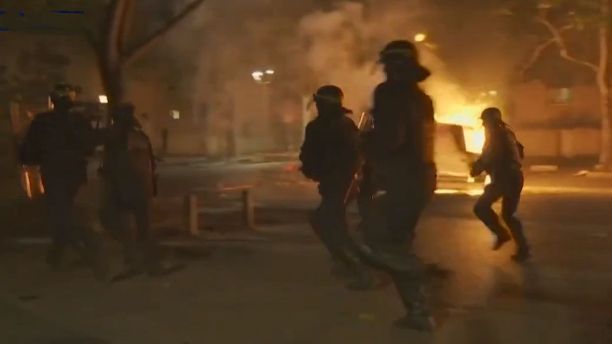 La polic&iacute;a corre entre el fuego por los autos incendiados en Nanterre. (Foto: Captura de TV)