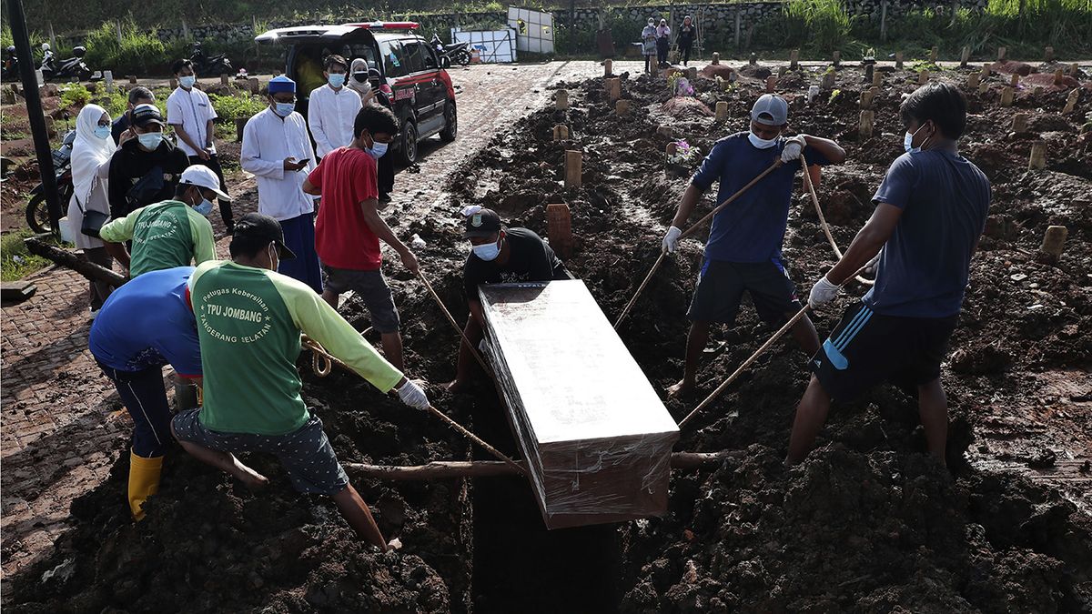 Unos trabajadores bajan un ataúd durante la inhumación de una víctima fatal de COVID-19, en una zona especial para esos cadáveres en el cementerio público de Jombang. (Foto: AP)