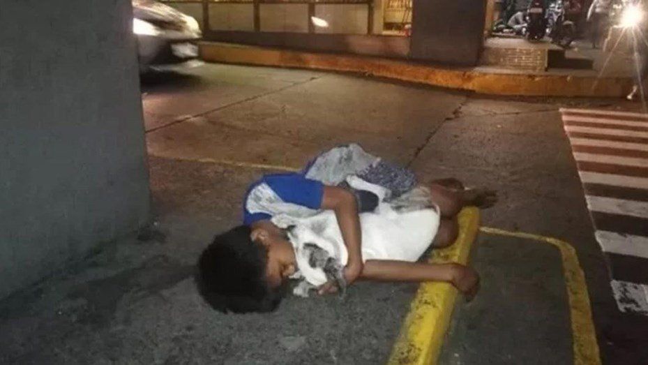 Un nene sin hogar duerme en la calle abrazado a su perro