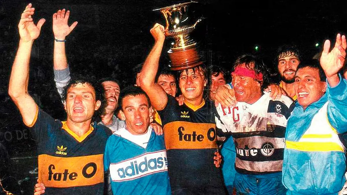 Jugadores de Boca festejando un campeonato, levantando una copa dorada en una noche de celebración, reflejando una era del fútbol con Fate. 