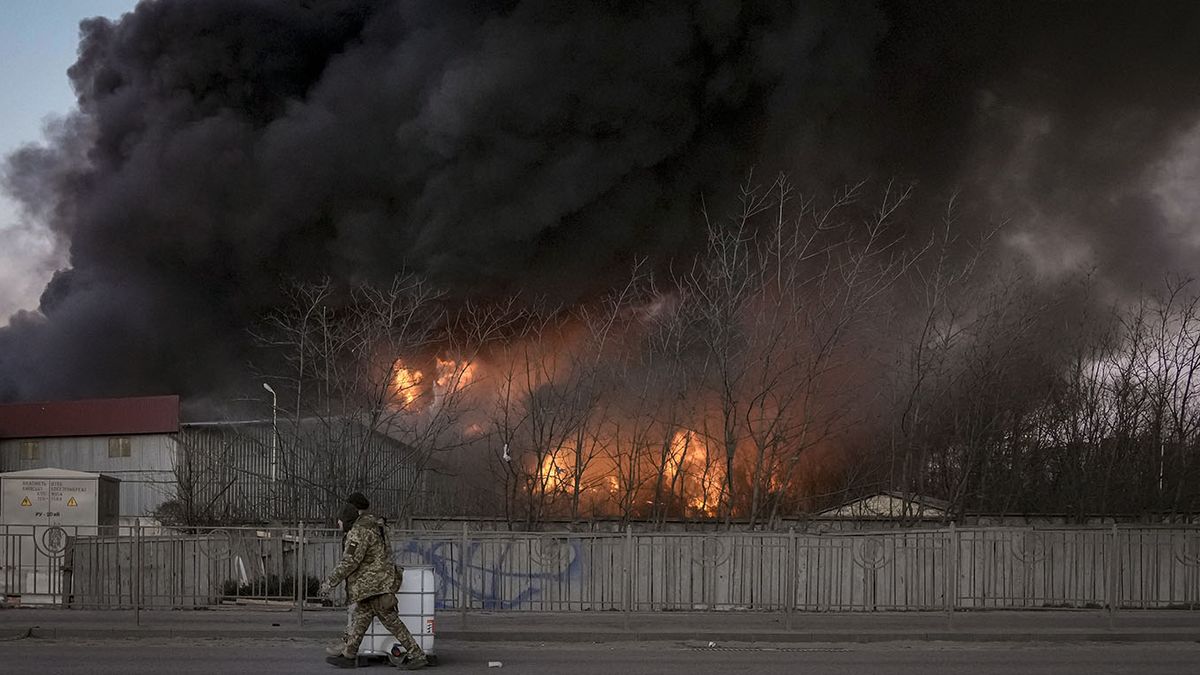 Soldados ucranianos que trasladan un contenedor pasan por delante de un incendio en un almacén tras un bombardeo