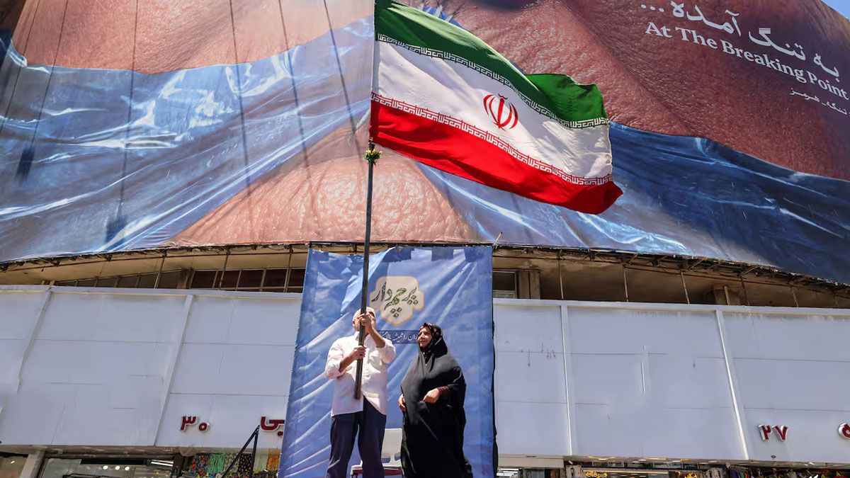 Un iraní hace flamear la bandera de su país delante del afiche enorme que muestra a Trump con la boca sellada. Teherán se siente 